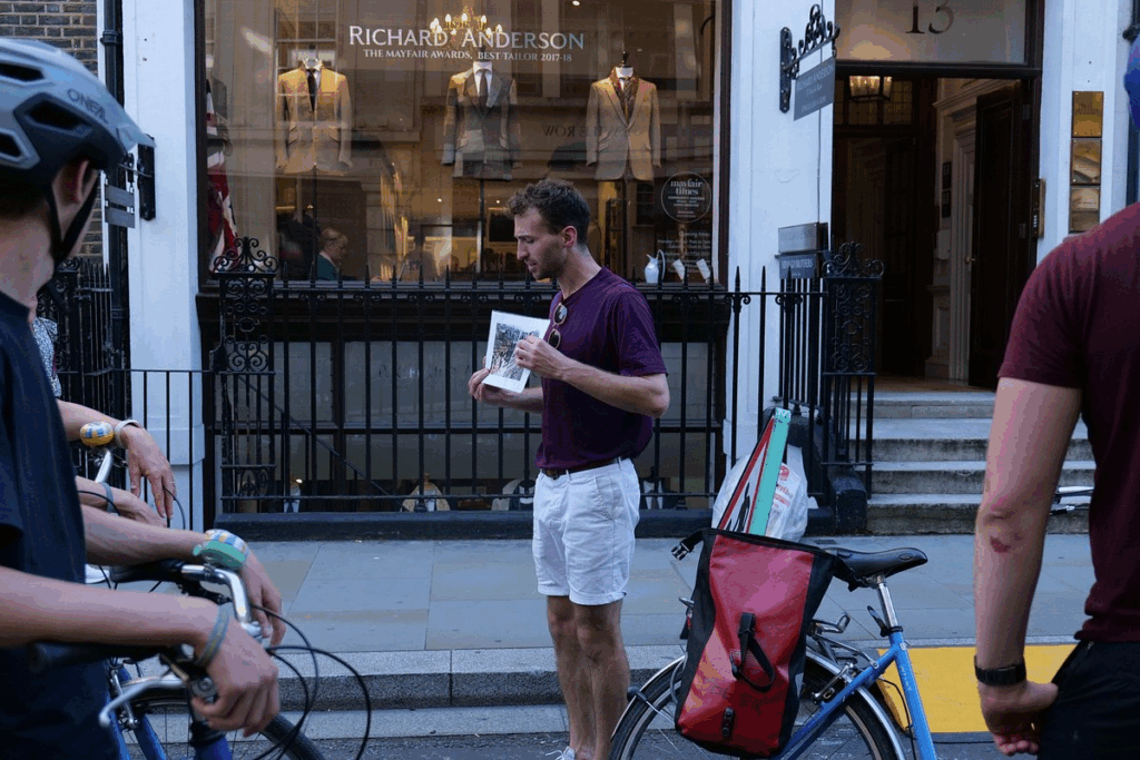 A cycling tour guide stopped in an old London street explaining the history to his group enjoying the best London tours