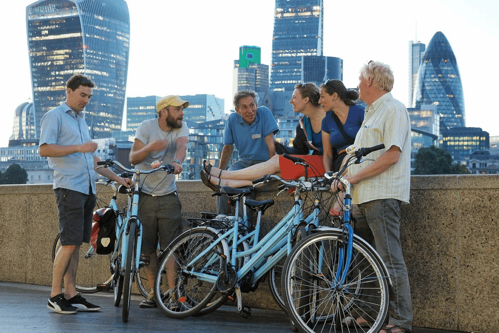 A small group of cyclists with their tour guide and a modern London landscape behind them enjoying the best London tours