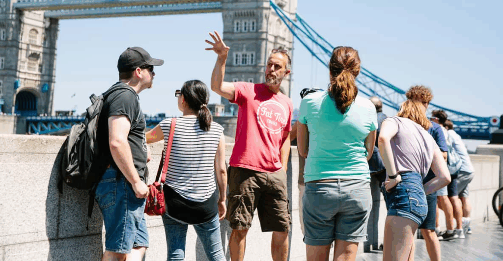 A small group of cyclists with their tour guide and the Tower Bridge behind them enjoying the best London tours