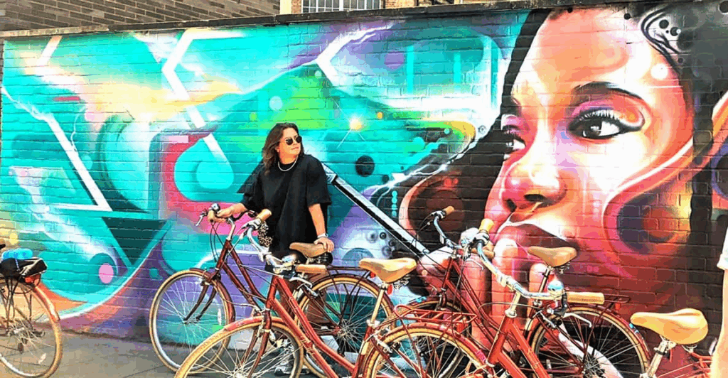 A group of bikes and a lone rider with dramatic artwork behind on a London Bike Tour