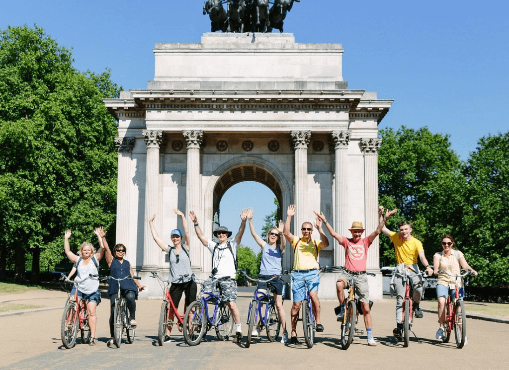 Group of cyclists celebrating beneath Wellington Arch in Hyde Park during london electric bike tours, enjoying a relaxed ride through one of the city’s most famous green spaces