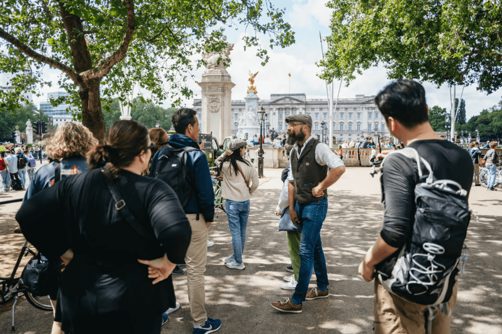 London bike tour guide explaining the history of Buckingham Palace to a group of cyclists gathered near the Victoria Memorial.