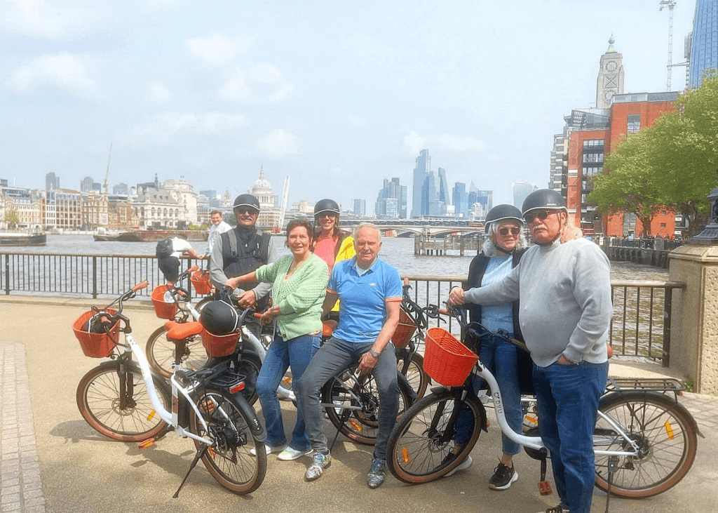 London bike tour guide posing with cyclists and rental bikes along the River Thames with the London skyline in the background.